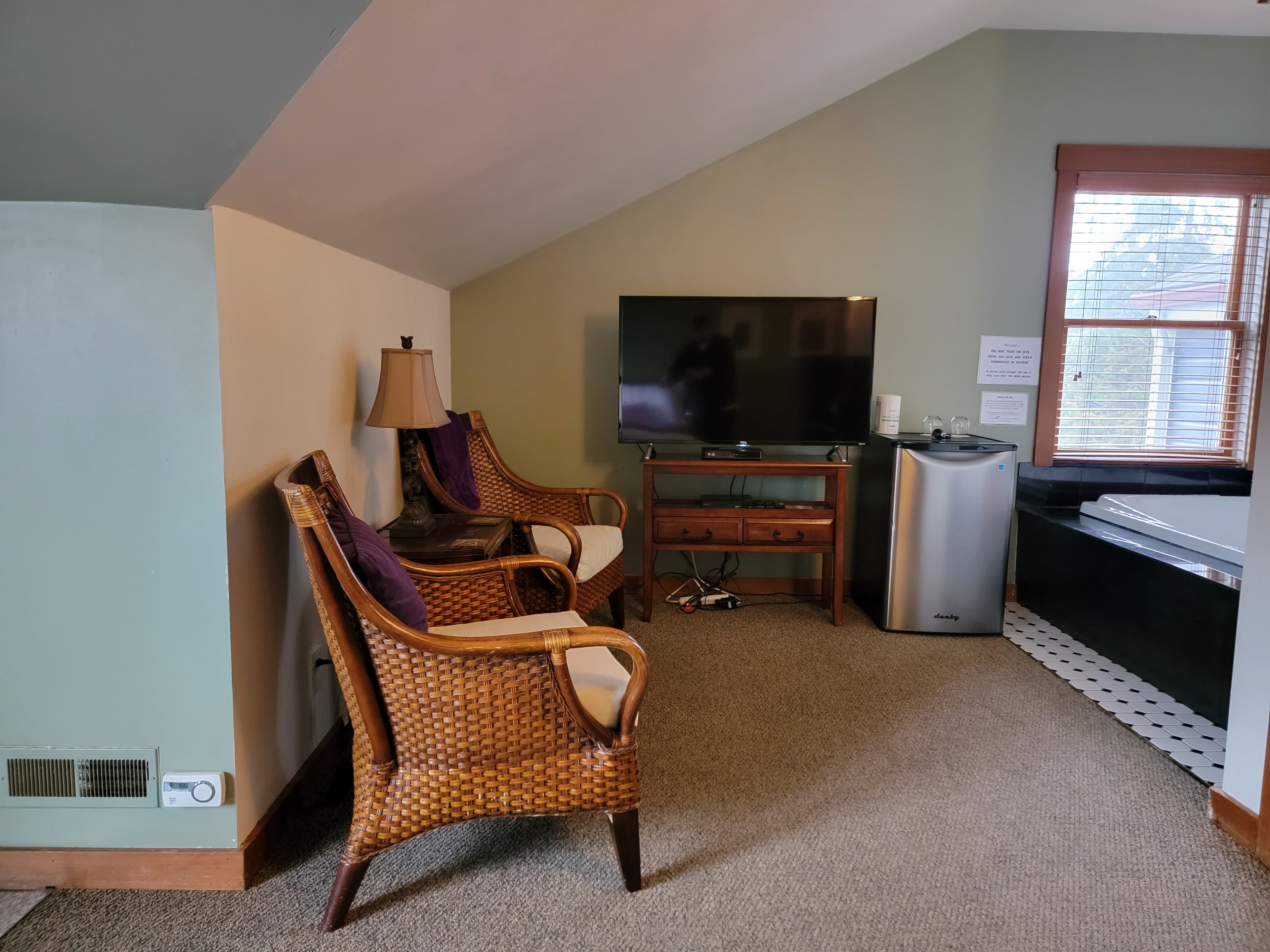 Cozy sitting area with wicker chairs, a television, and a small fridge in a room with sloped ceiling.