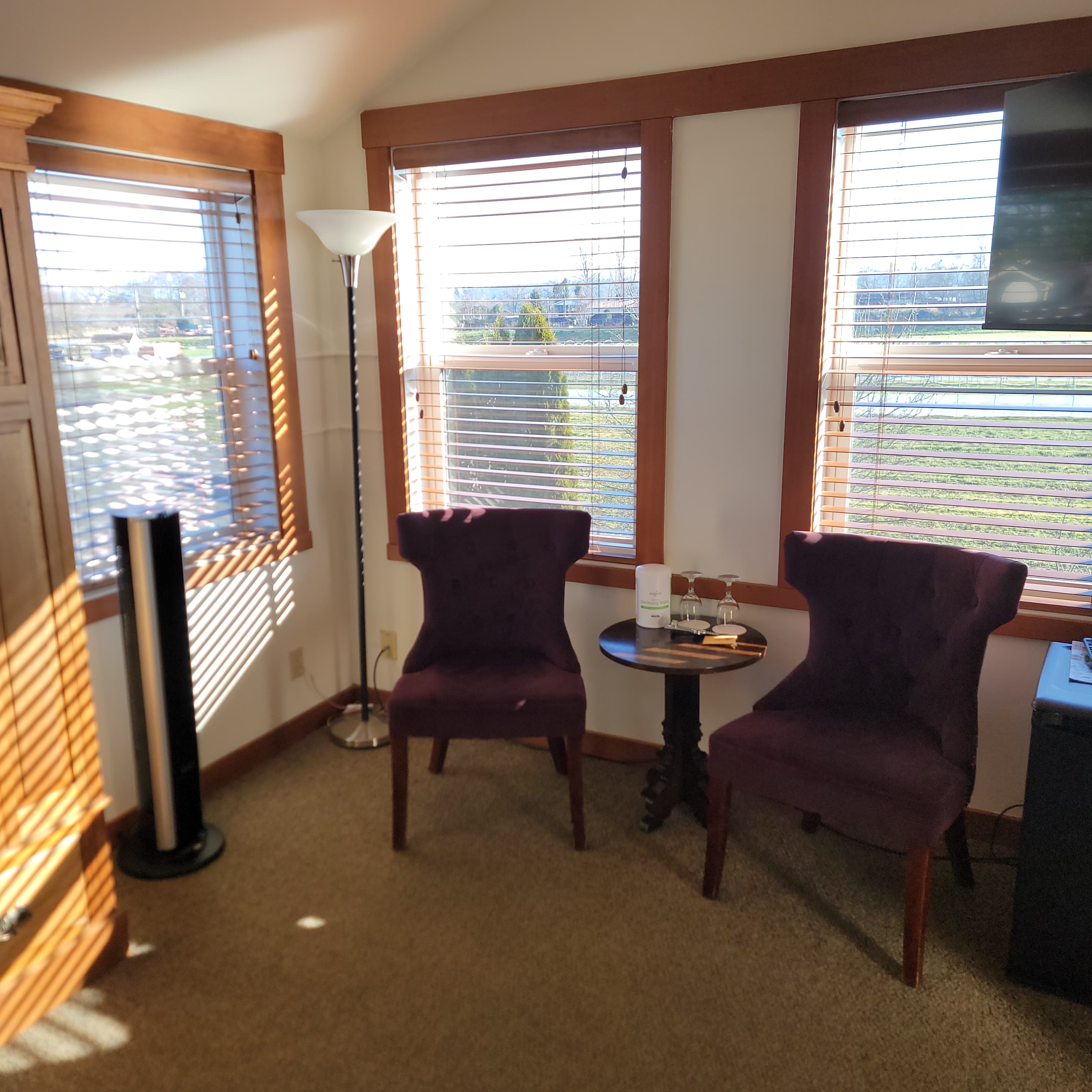 A cozy corner with two purple chairs, a small table, and natural light streaming through the blinds.