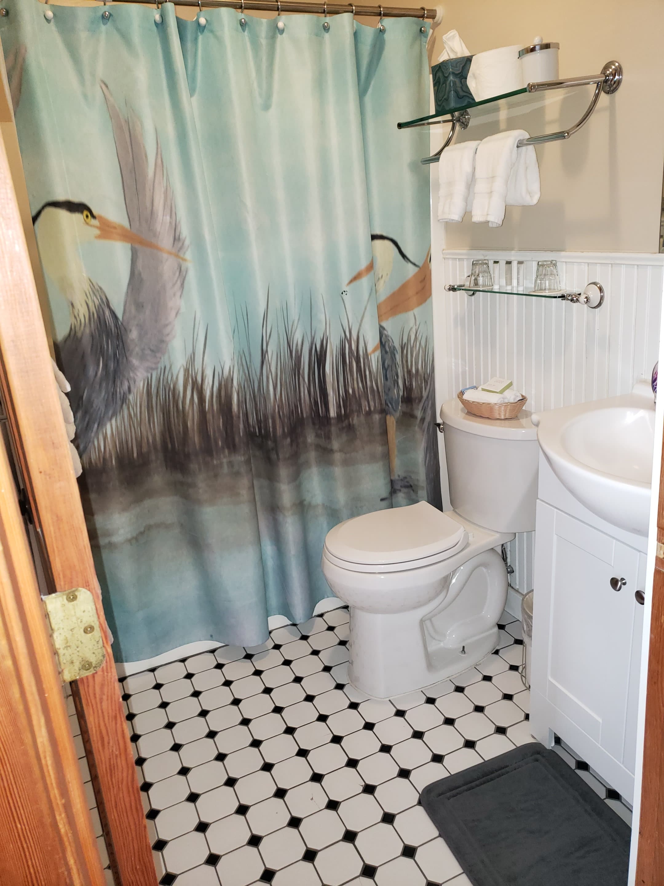 A small bathroom featuring a heron-themed shower curtain, a white toilet, and a sink with towels.