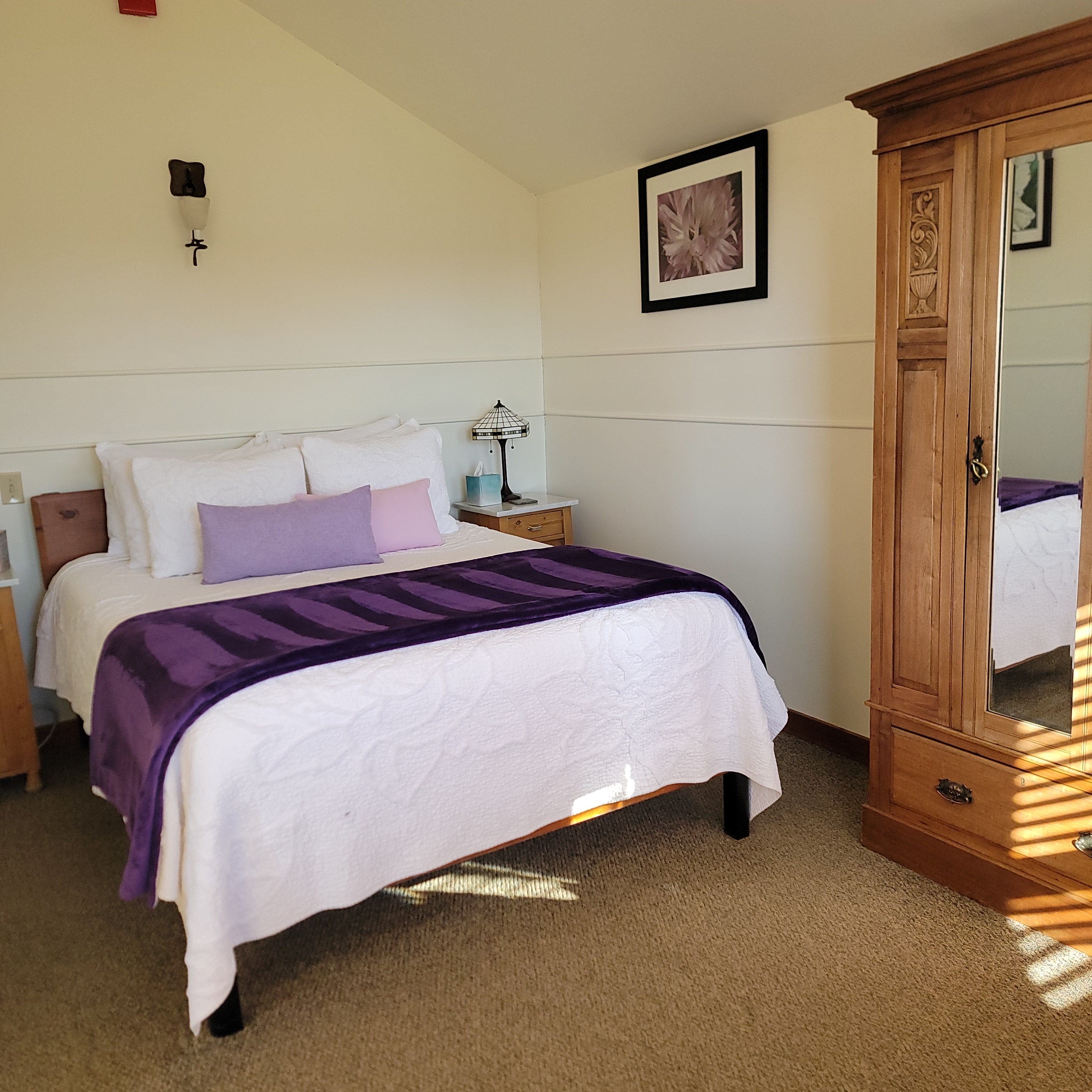 A cozy bedroom featuring a bed with purple accents, a wooden wardrobe, and decorative wall art.