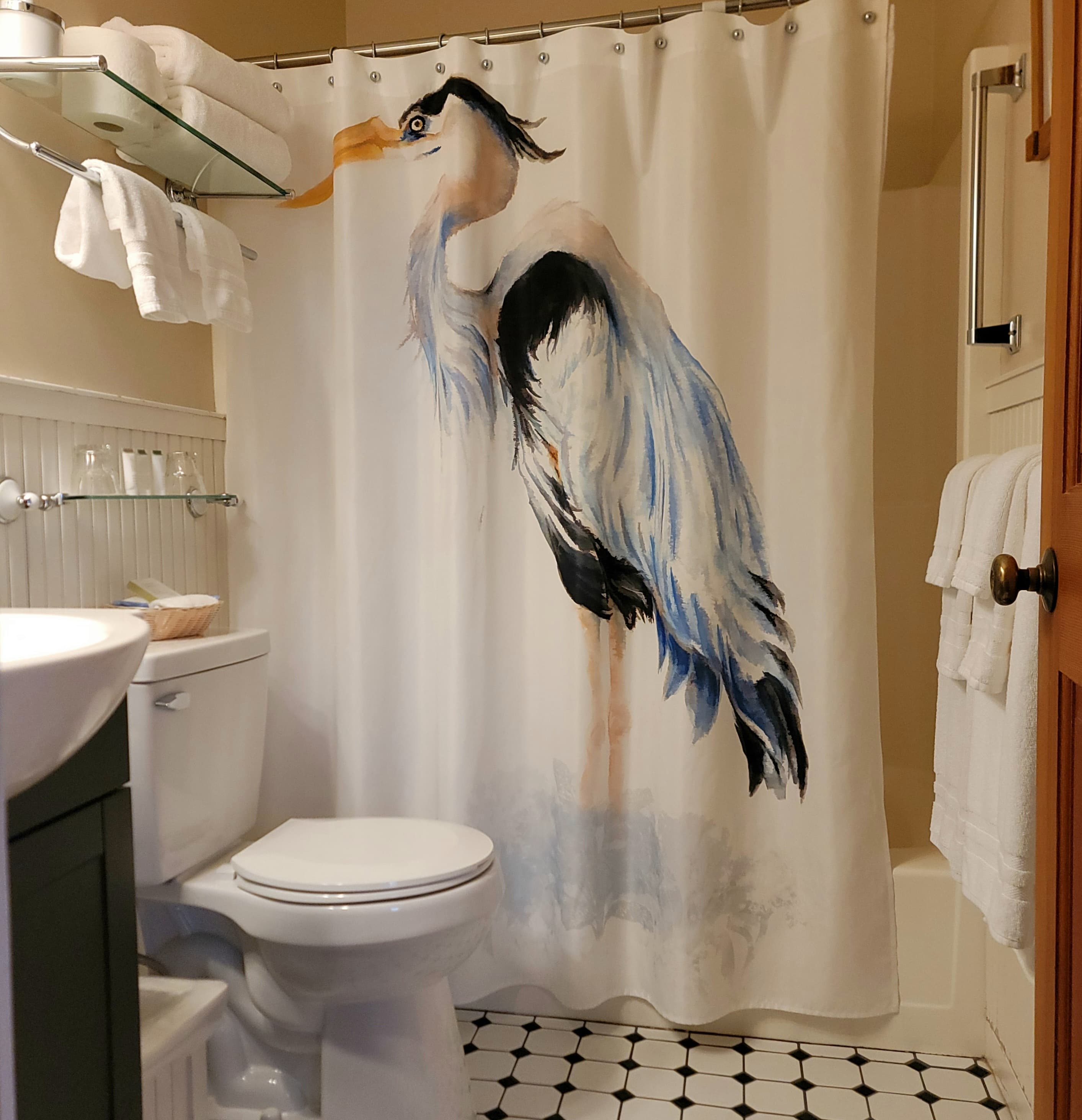 A bathroom with a shower curtain featuring a painted heron, a toilet, and neatly arranged towels.