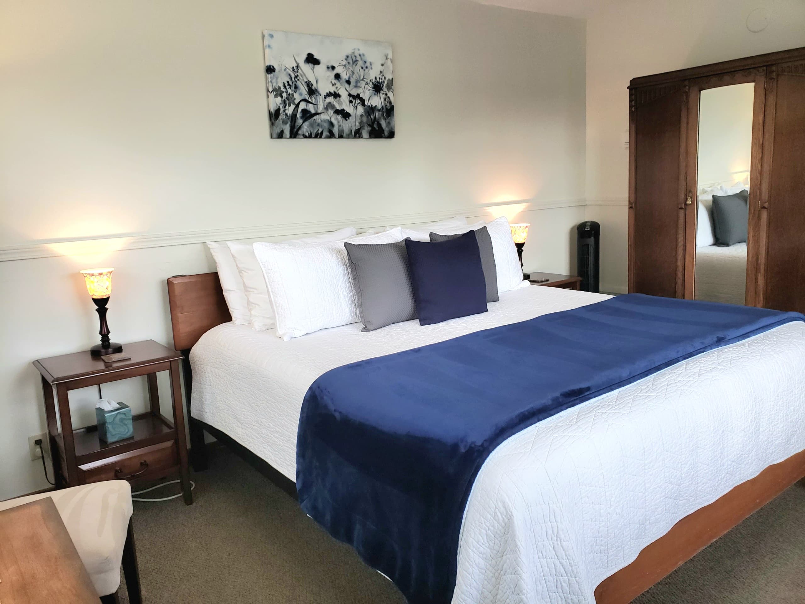 A cozy bedroom featuring a neatly made bed with pillows and a navy blue throw, flanked by two lamps and wooden furniture.