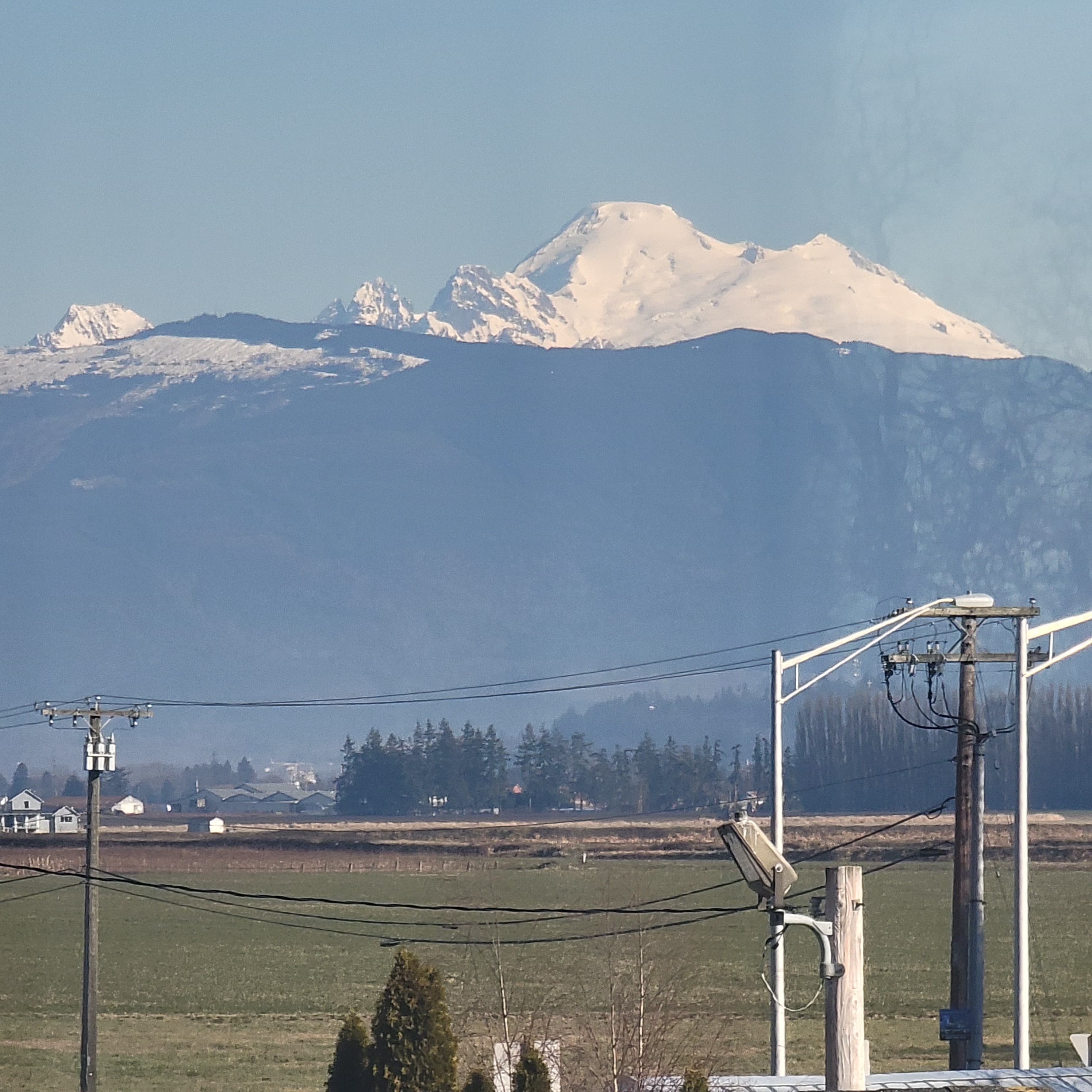 A snow-capped mountain range looms in the distance, framed by telephone poles and farmland.