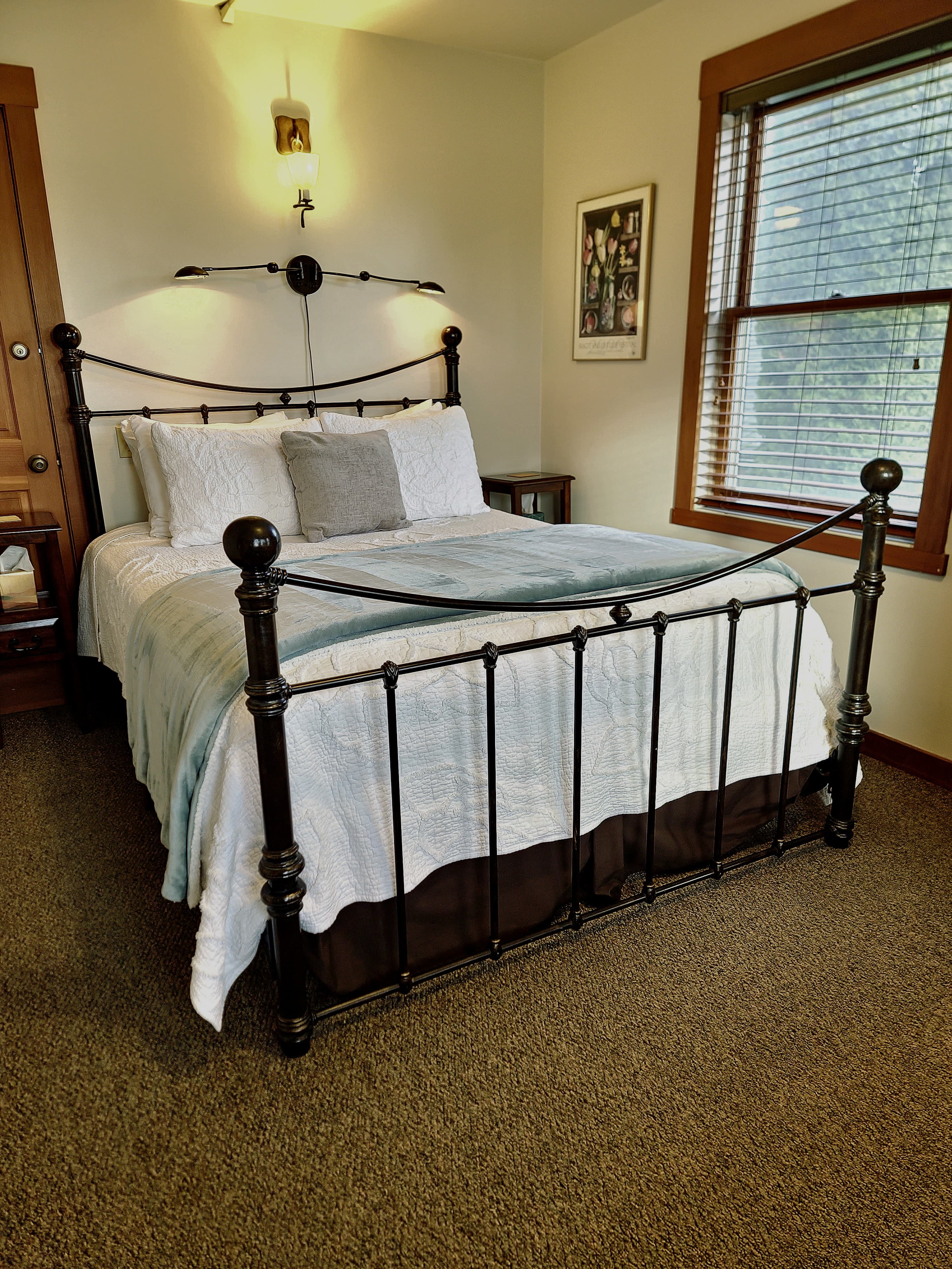 A cozy bedroom featuring a black metal bed frame with white linens and a blue throw blanket against a neutral wall.