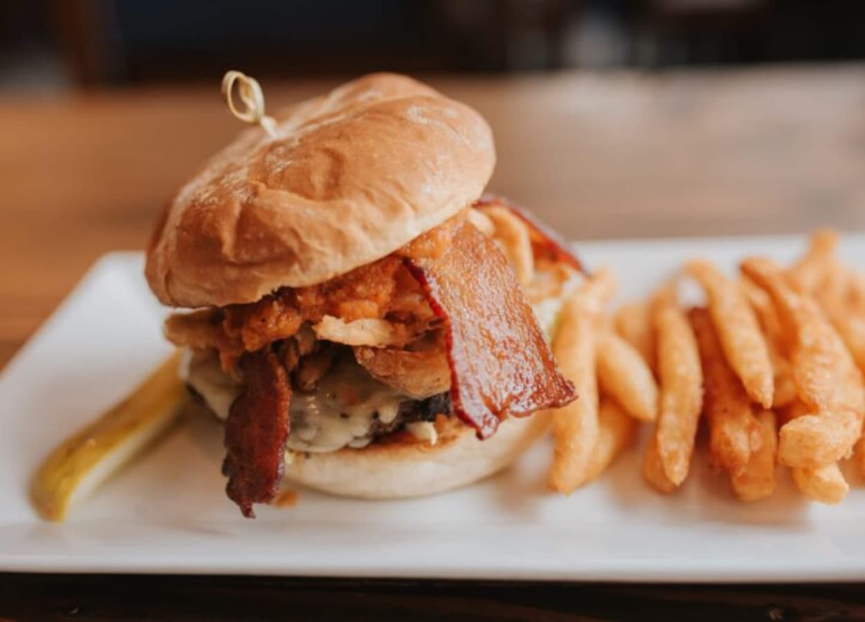 A hearty burger topped with bacon and crispy onions, served with crinkle-cut fries and a pickle.