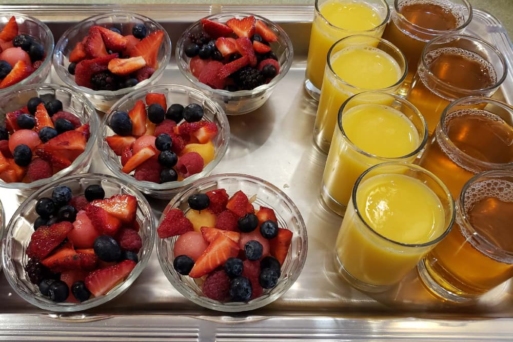 A tray featuring bowls of mixed fresh fruit and glasses of yellow and brown beverages.