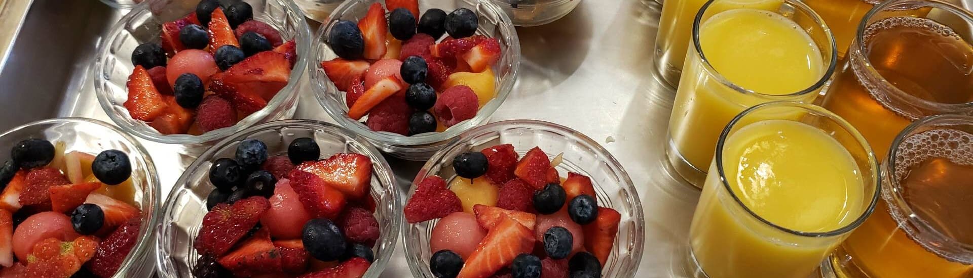 A tray featuring bowls of mixed fresh fruit alongside glasses of orange juice and a dark beverage.