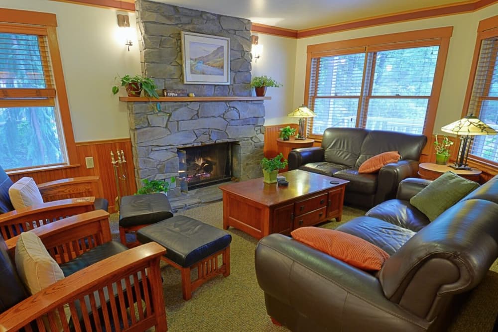 Cozy living room featuring a stone fireplace, wooden furniture, and large windows.