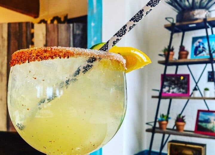 A refreshing margarita with a salted rim, garnished with lemon and a decorative straw.