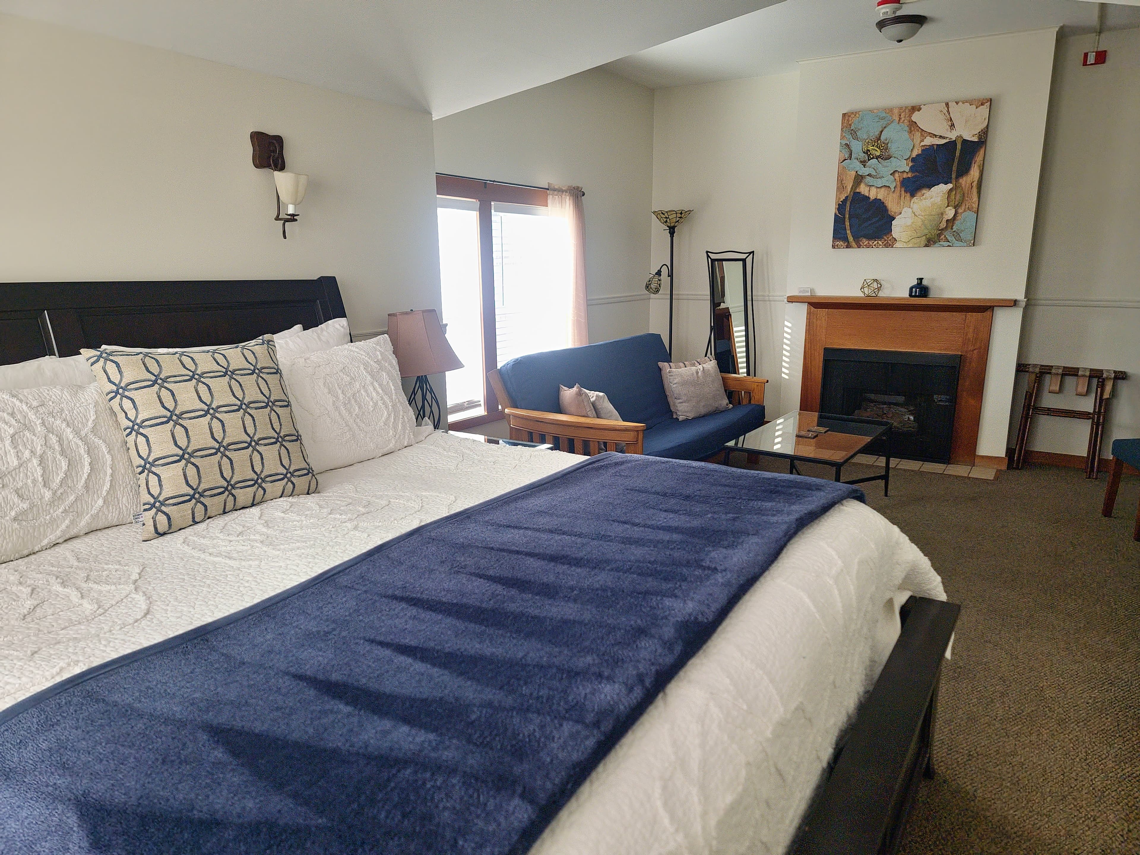 A stylish bedroom featuring a large bed, blue throw blanket, cozy seating area, and a fireplace.