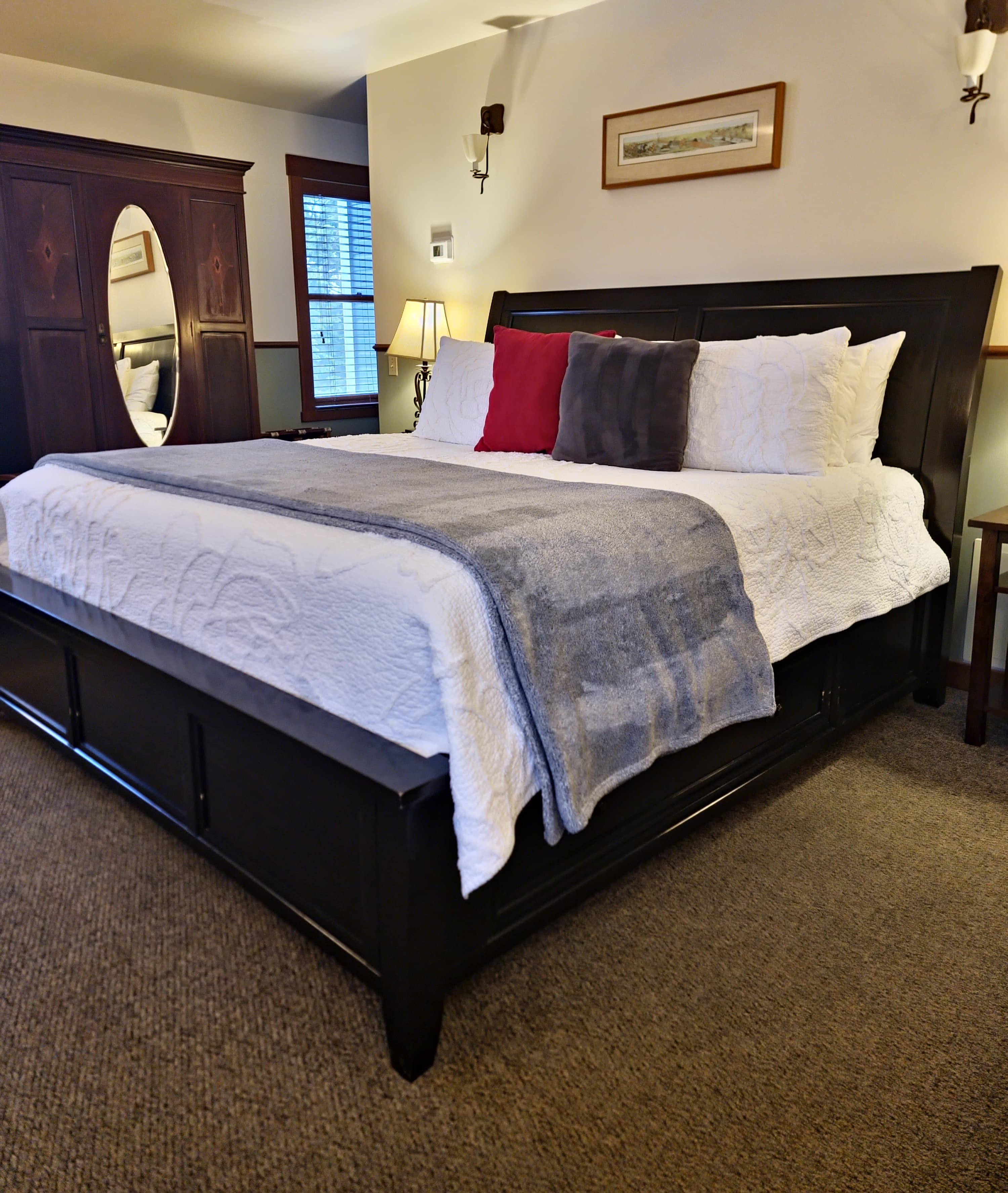 A cozy bedroom featuring a large bed with decorative pillows and a dark wooden wardrobe in the background.