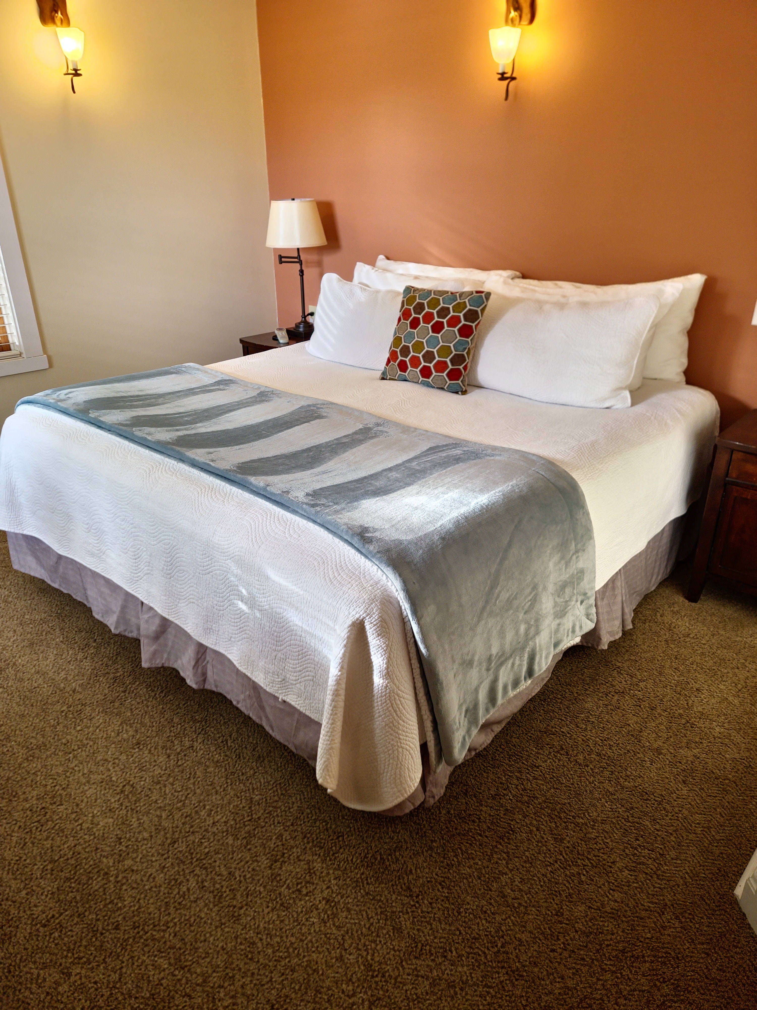 A neatly made bed with a decorative pillow, soft blankets, and warm wall lighting in a cozy room.